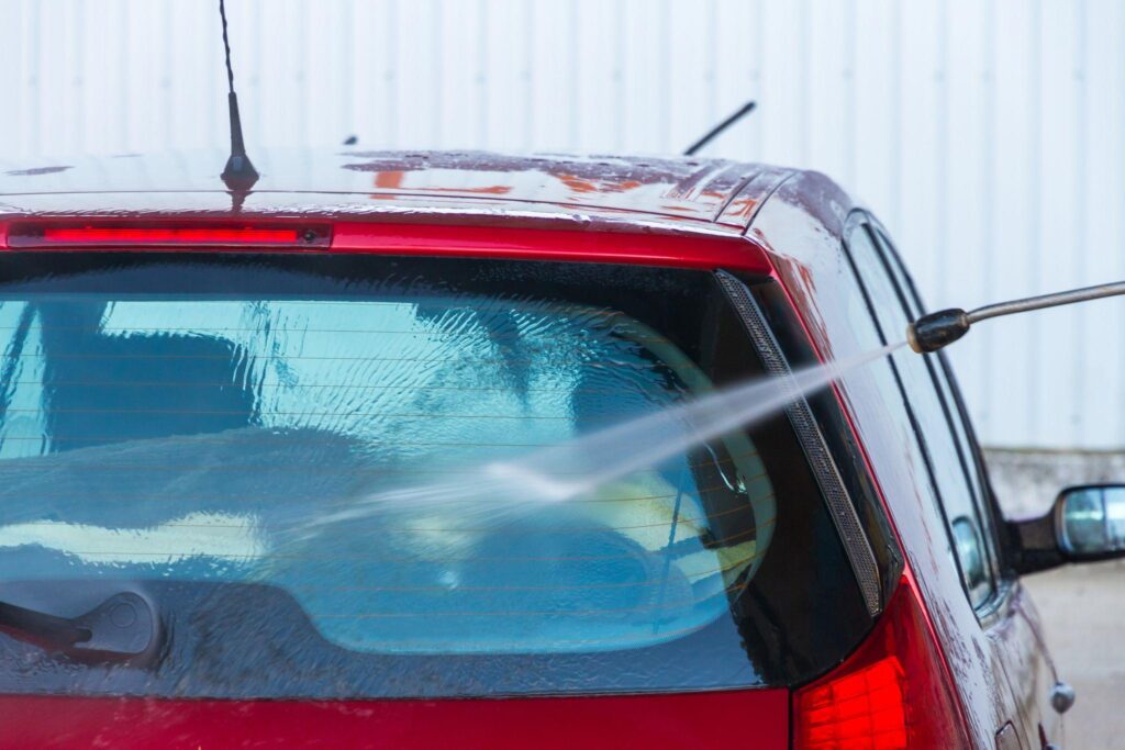 A power-washer spraying the rear windshield of a red vehicle